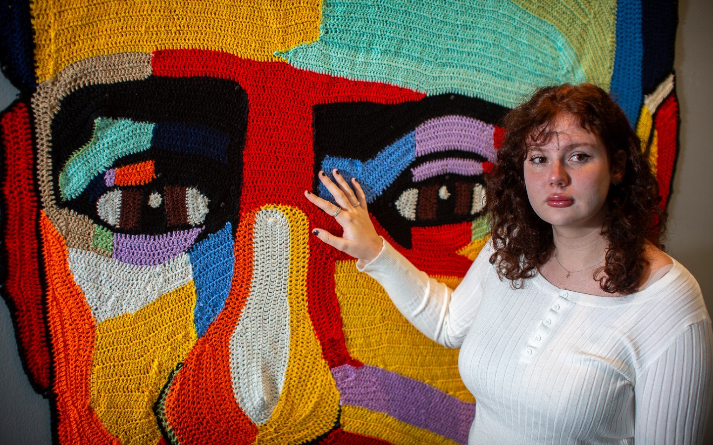 A young woman standing in front of a colourful artwork. 